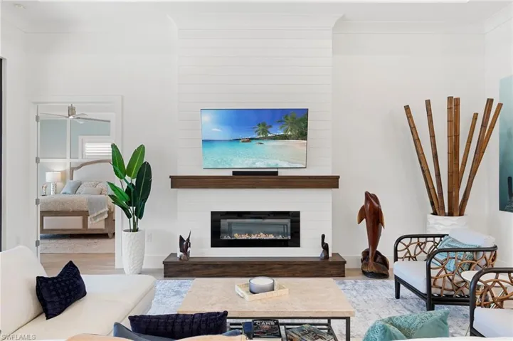 Living area with a large fireplace, ceiling fan, ornamental molding, and wood finished floors