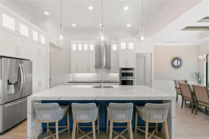 Kitchen with a large island, wall chimney exhaust hood, ornamental molding, stainless steel appliances, and a sink