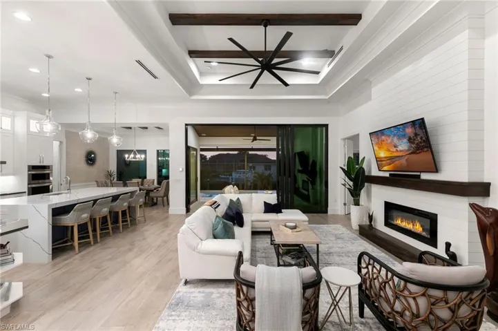 Living room with a glass covered fireplace, beam ceiling, light wood-style flooring, and ceiling fan with notable chandelier