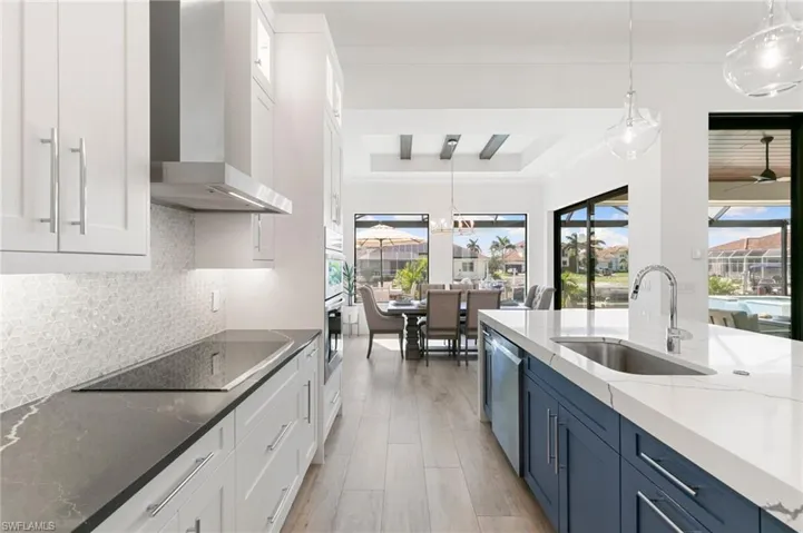 Kitchen with blue cabinets, stainless steel appliances, a sink, a ceiling fan, and wall chimney exhaust hood