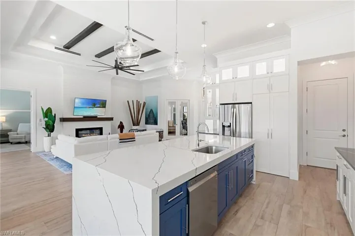 Kitchen with stainless steel appliances, a sink, white cabinets, blue cabinetry, and a glass covered fireplace