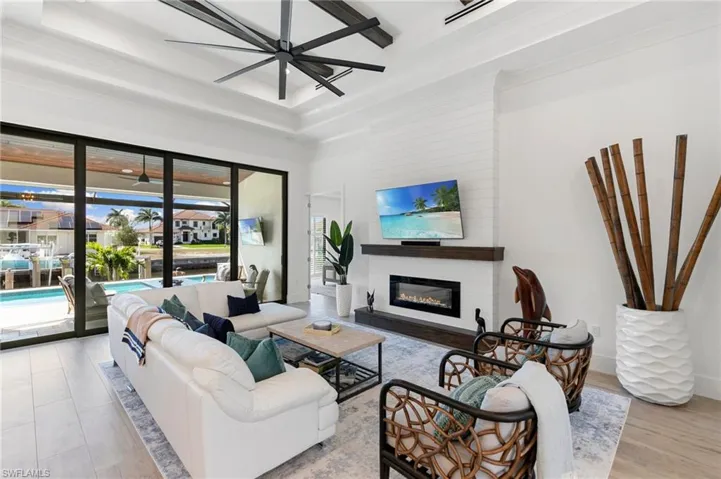 Living room featuring a tray ceiling, a glass covered fireplace, baseboards, and wood finished floors