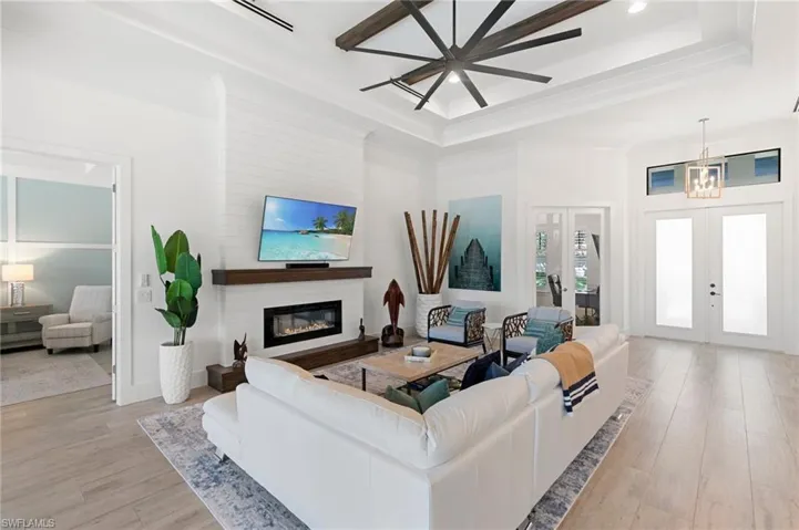 Living room with light wood-style floors, a tray ceiling, a glass covered fireplace, and french doors