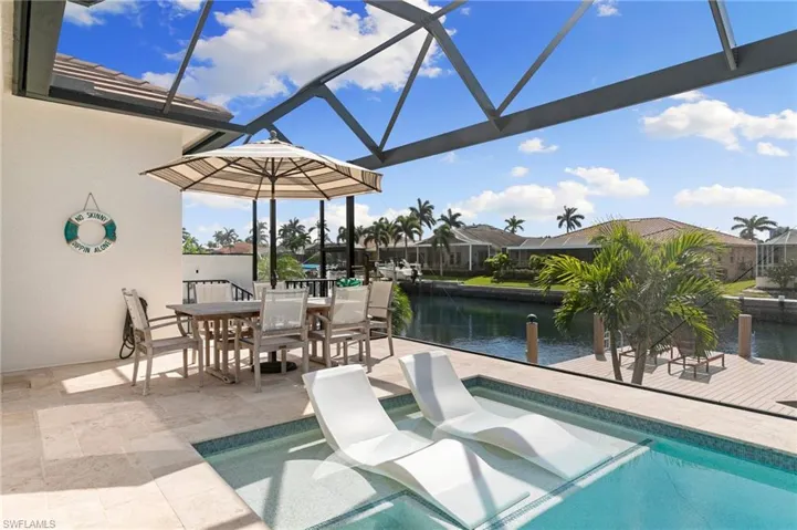 View of pool with a patio area, glass enclosure, outdoor dining space, and a water view