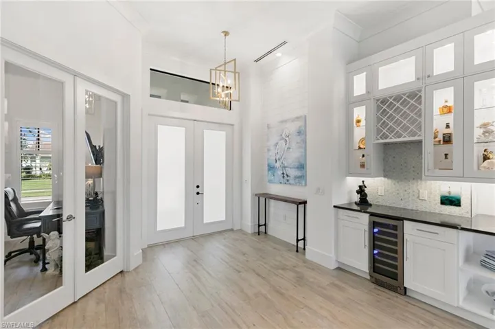 Entrance foyer with beverage cooler, light wood finished floors, french doors, ornamental molding, and a bar