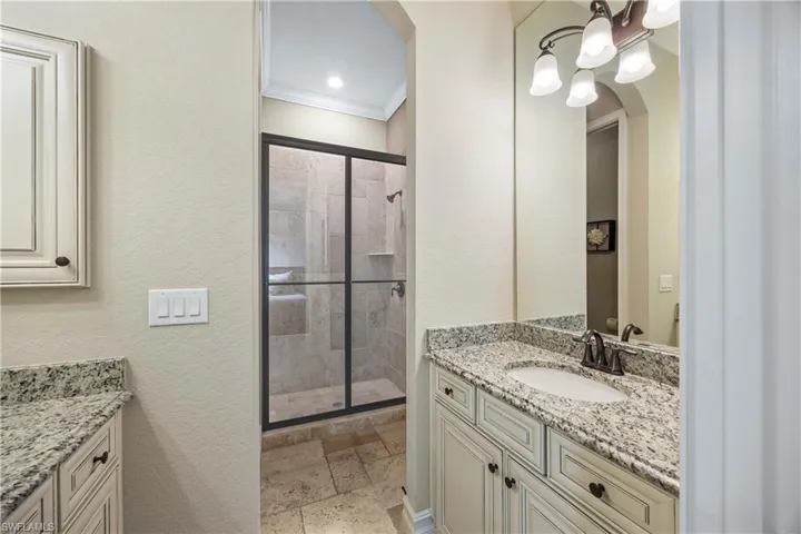 Full bathroom with vanity, stone tile flooring, a textured wall, crown molding, and a stall shower