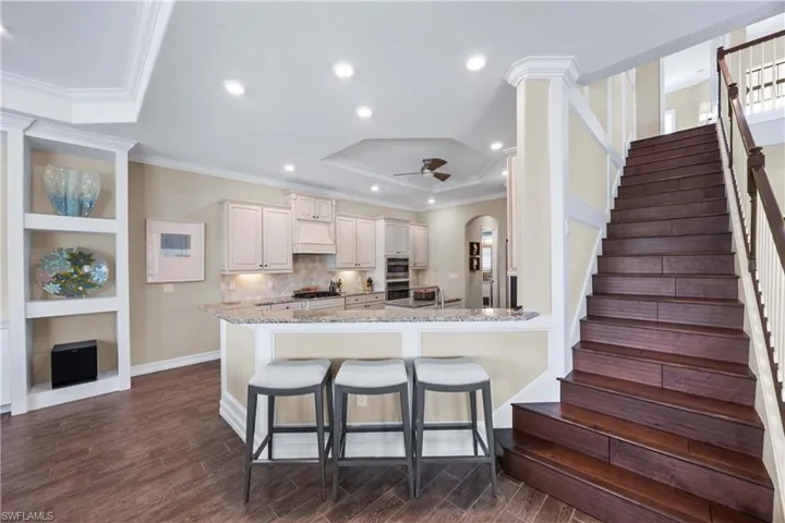 Kitchen with a kitchen breakfast bar, light stone countertops, built in features, wood finish floors, and arched walkways