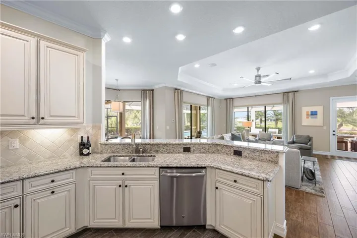 Kitchen with ornamental molding, open floor plan, a peninsula, stainless steel dishwasher, and light stone counters