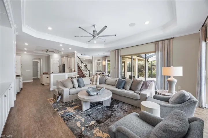 Living area with a ceiling fan, ornamental molding, wood finished floors, arched walkways, and a raised ceiling