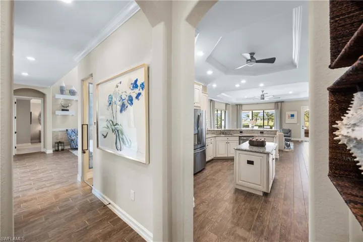 Hallway featuring arched walkways, ornamental molding, dark wood-style flooring, recessed lighting, and a raised ceiling