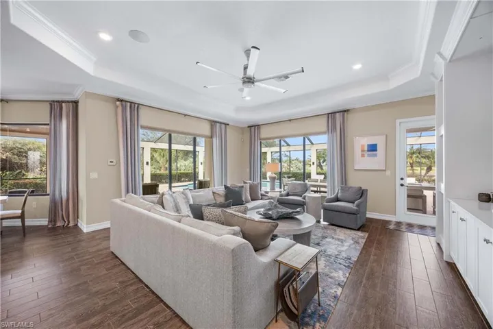 Living area featuring dark wood finished floors, a ceiling fan, ornamental molding, a raised ceiling, and recessed lighting