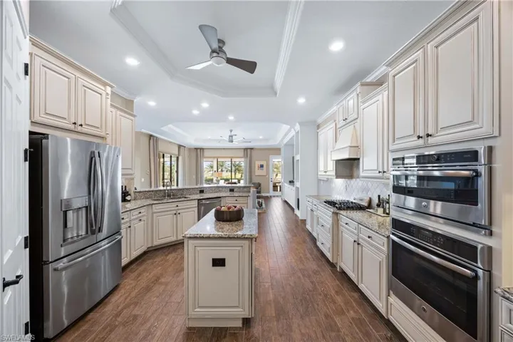 Kitchen featuring a raised ceiling, a peninsula, appliances with stainless steel finishes, ornamental molding, and light stone counters