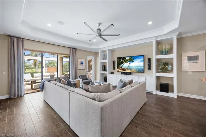 Living area with a ceiling fan, dark wood-style floors, built in features, a tray ceiling, and ornamental molding