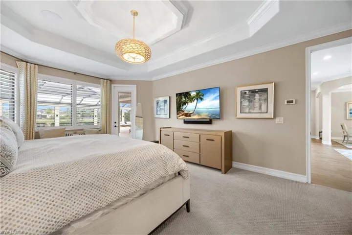 Bedroom featuring access to outside, arched walkways, carpet floors, ornamental molding, and a tray ceiling