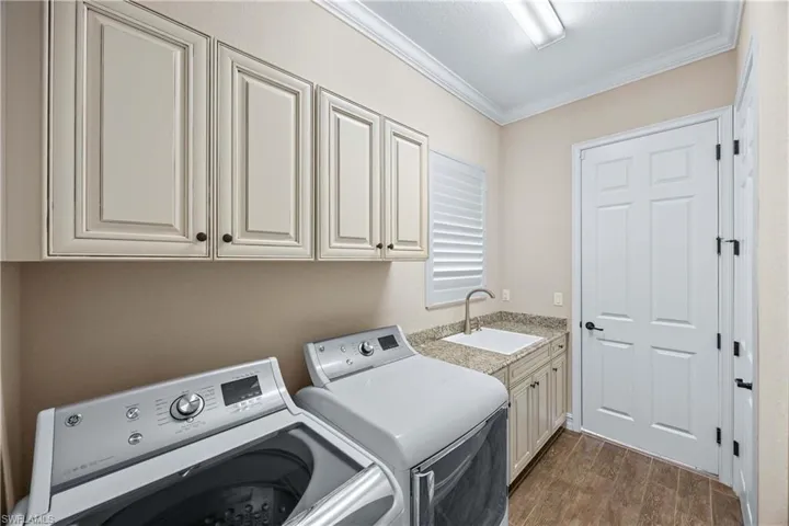 Laundry room with dark wood-style floors, crown molding, independent washer and dryer, and cabinet space