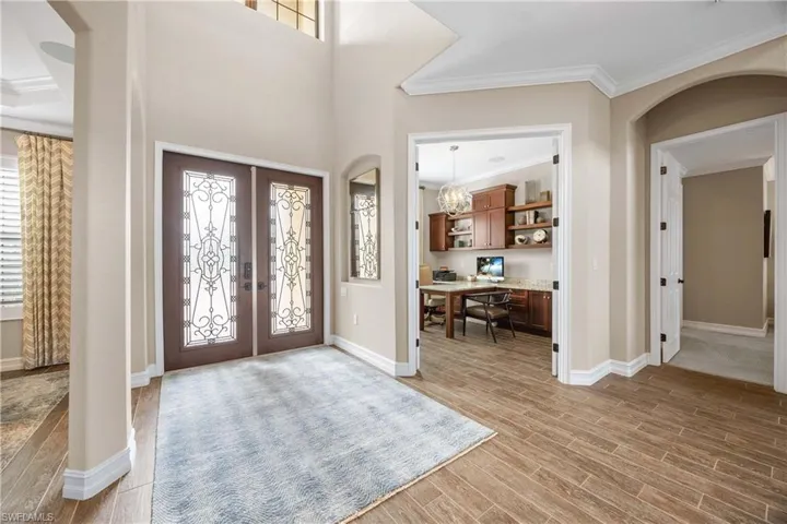 Foyer entrance with arched walkways, ornamental molding, wood tiled floors, french doors, and a chandelier