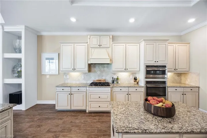 Kitchen featuring light stone countertops, dark wood-type flooring, double oven, crown molding, and premium range hood