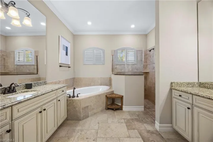 Full bathroom with stone tile flooring, a bath, two vanities, walk in shower, and crown molding