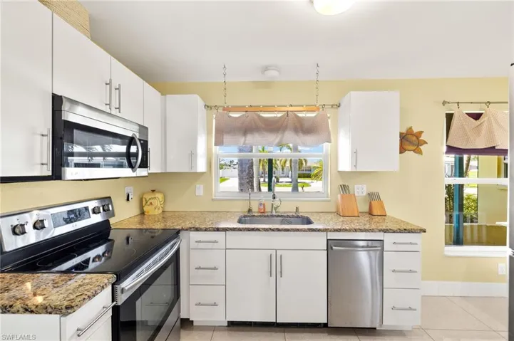 Kitchen with white cabinets, light stone counters, appliances with stainless steel finishes, and a sink