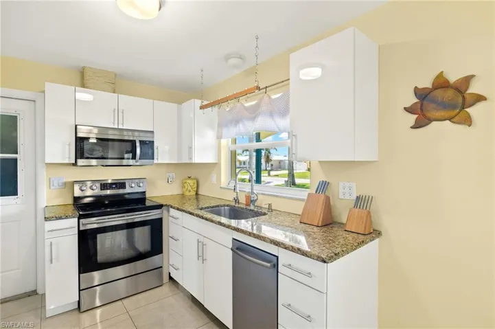 Kitchen with light tile patterned floors, appliances with stainless steel finishes, stone counters, a sink, and white cabinetry