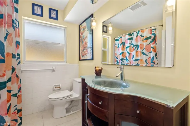 Full bathroom with tile patterned floors, tile walls, toilet, vanity, and visible vents