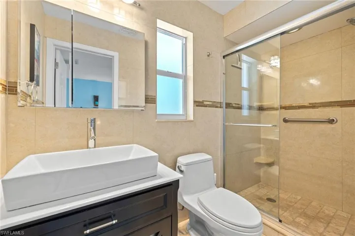Bathroom with toilet, vanity, a shower stall, and tile walls