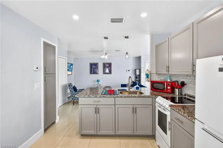 Kitchen featuring gray cabinetry, white appliances, a peninsula, recessed lighting, and light stone countertops