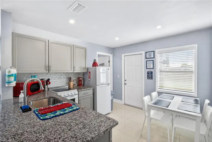 Kitchen featuring gray cabinets, dark stone counters, decorative backsplash, white appliances, and light tile patterned floors