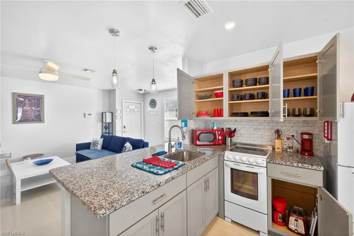 Kitchen with light stone counters, a peninsula, white appliances, pendant lighting, and open floor plan