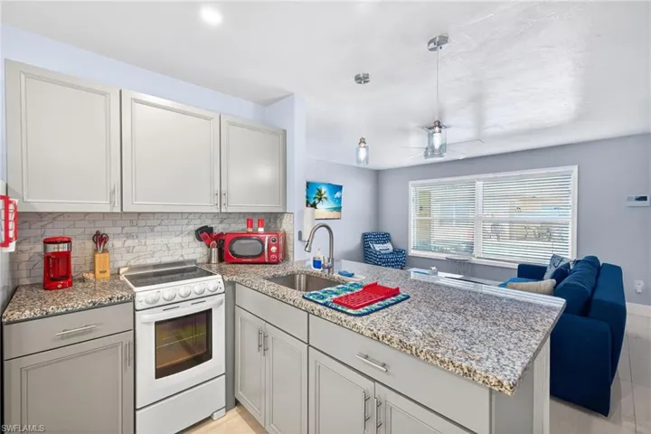 Kitchen with a peninsula, electric range, light stone countertops, backsplash, and hanging light fixtures