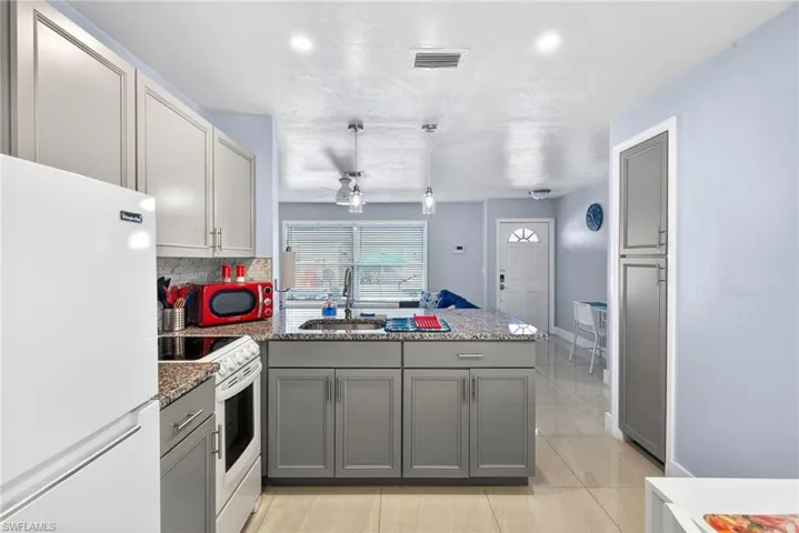 Kitchen featuring white appliances, a peninsula, dark stone counters, hanging light fixtures, and gray cabinets