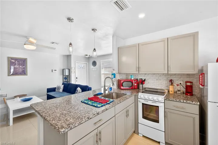 Kitchen with light stone counters, white appliances, a peninsula, decorative light fixtures, and open floor plan