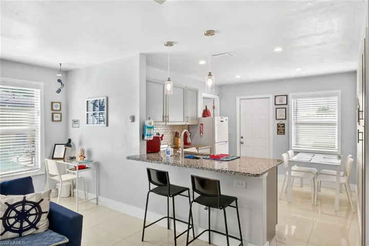 Kitchen with a breakfast bar, a peninsula, light stone countertops, tasteful backsplash, and decorative light fixtures