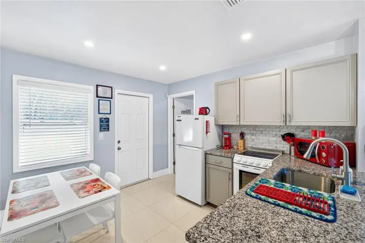 Kitchen with white appliances, backsplash, light stone countertops, recessed lighting, and gray cabinetry