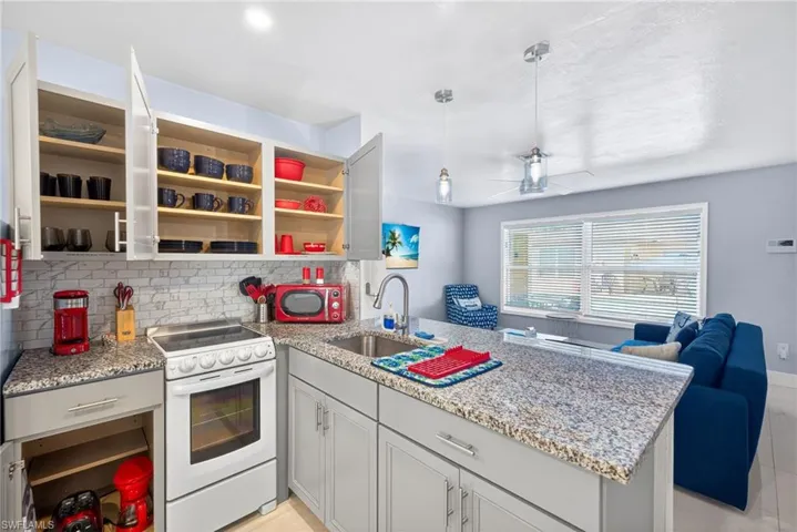 Kitchen featuring a peninsula, white electric range oven, light stone counters, tasteful backsplash, and open floor plan