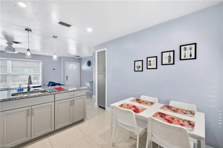 Kitchen featuring light stone counters, gray cabinetry, light tile patterned flooring, and hanging light fixtures