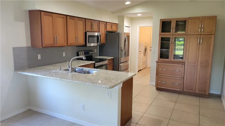 Kitchen featuring light wood cabinetry, stainless steel appliances, granite countertops, tile flooring, and a gray tile backsplash