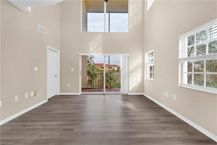 Unfurnished living room with a towering ceiling, baseboards, visible vents, and wood finished floors