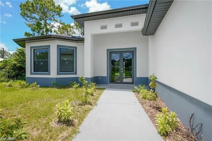View of exterior entry featuring french doors, stucco siding, and a yard