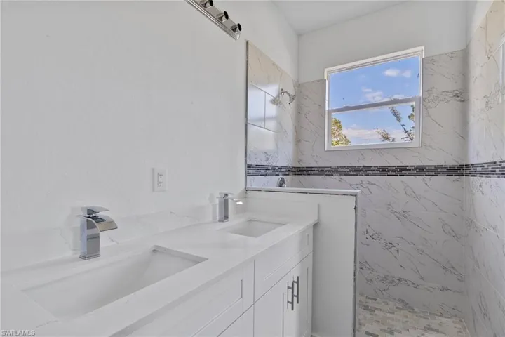 Bathroom with walk in shower, double vanity, and tile walls