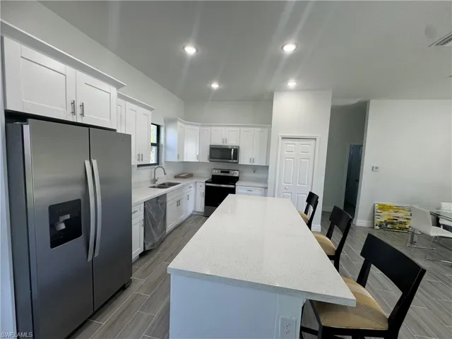Kitchen featuring stainless steel appliances, a sink, a kitchen island, white cabinets, and a kitchen bar