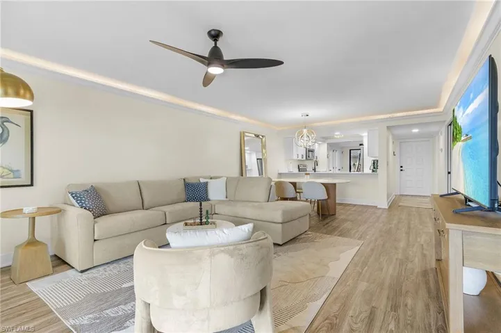 Living room with ornamental molding, light wood-type LVT flooring, and ceiling fan