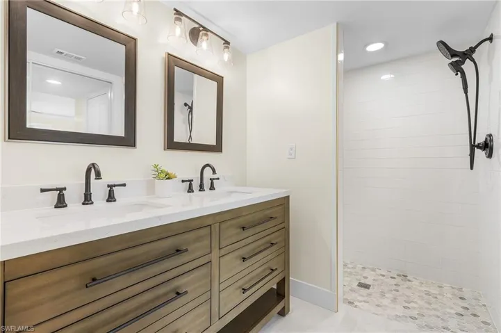 Master bathroom with dual sink vanity, tiled shower, and custom tile