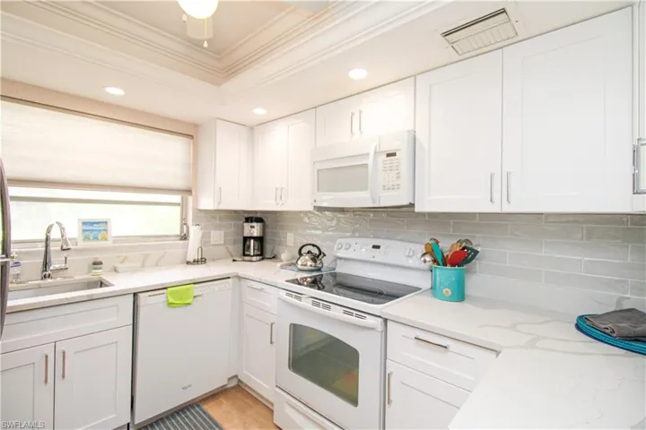 Kitchen featuring white appliances, decorative backsplash, light wood-type flooring, sink, and white cabinetry