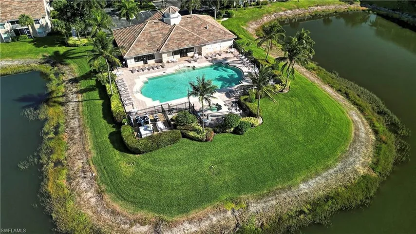 Resort-style pool area featuring an irregular-shaped pool, surrounding sun deck, mature palm trees, and manicured landscaping
