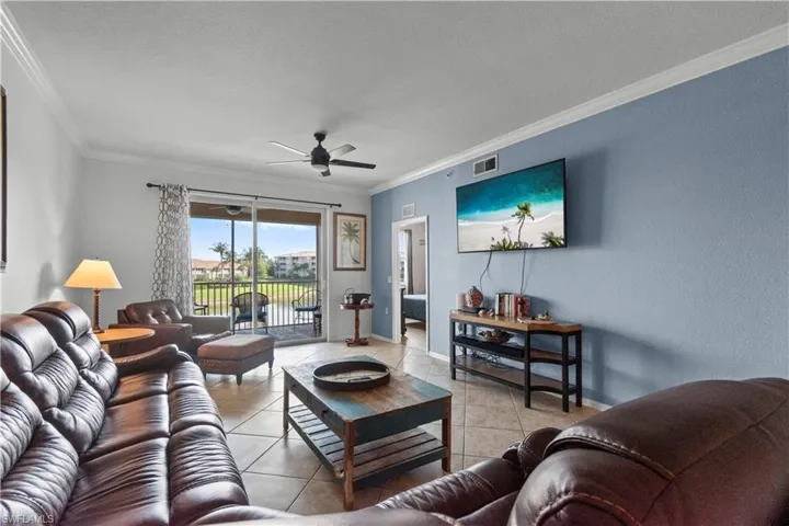 Spacious living area featuring neutral tile flooring, a ceiling fan, and crown molding