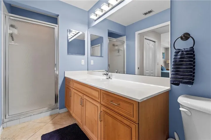 Primary bathroom featuring a shower with frosted glass enclosure, a wood-finish vanity with a white countertop, a large wall-mounted mirror, and tile flooring