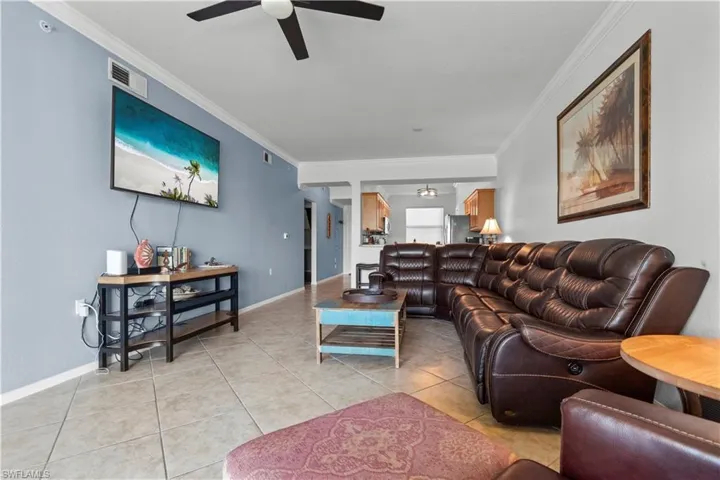 Spacious living area featuring tiled flooring, a ceiling fan, crown molding, and a wall-mounted television