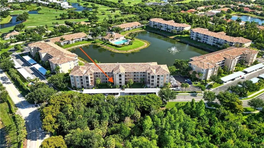 Multi-story residential building with a tile roof, surrounded by mature trees, and featuring a manicured golf course backdrop