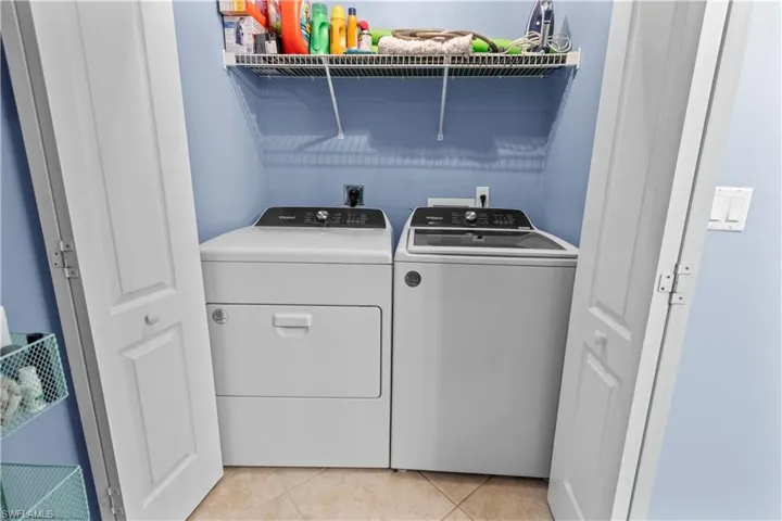 Dedicated laundry area featuring a washer and dryer, tiled flooring, light blue walls, and a white wire shelving unit